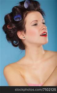 Girl preparing to party. Headshot of young woman with hair curlers pin up makeup studio shot on blue
