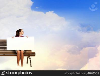 Girl presenting something. Young woman with white blank banner sitting on bench