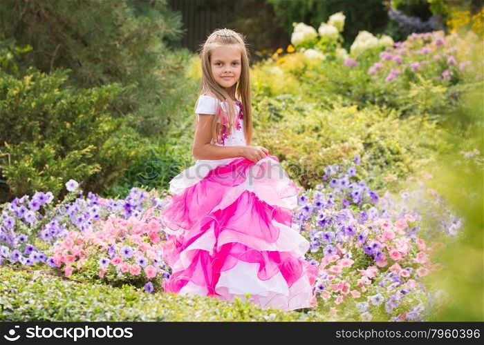 Girl Princess in the garden flower bed. Happy six year old girl in a lush evening pink dress walking through the green garden