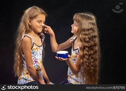 Girl puts cream on her sister's nose