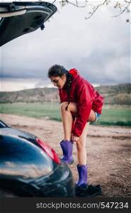 Girl putting her waterproof boots near her car.
