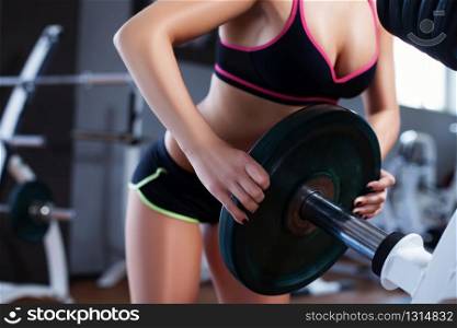 Girl putting weight plate on the bar. Girl in the gym