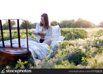 girl reading a book in bed among the fields at sunset
