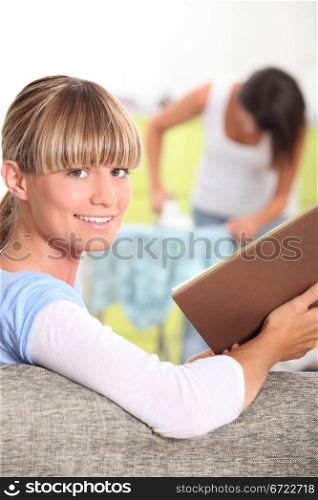 girl reading a book while her mother is ironing