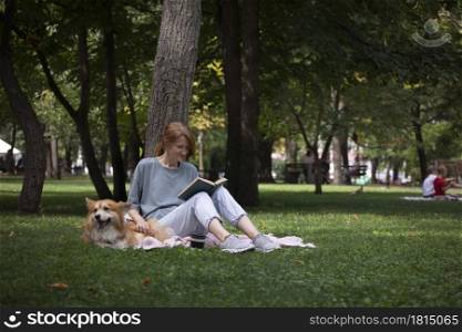 girl reading a book with dog corgi on the lawn