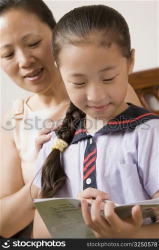 Girl reading a book with her mother behind her and smiling