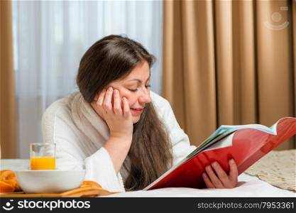 girl reading an interesting magazine on bed in bathrobe
