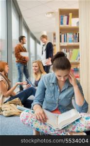 Girl reading book with group of students discussing in library