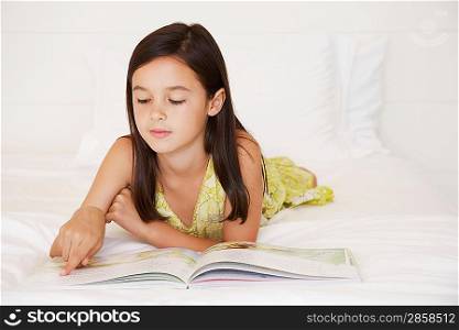 Girl reading story book lying on bed