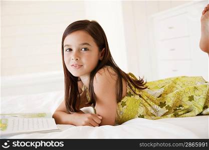 Girl reading story book lying on stomach on bed