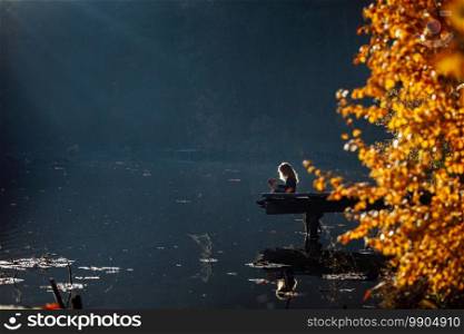 girl reads a book in autumn by the river. lonely young woman reads a book on a wooden bridge.. girl reads a book in autumn by the river. lonely young woman reads a book on a wooden bridge