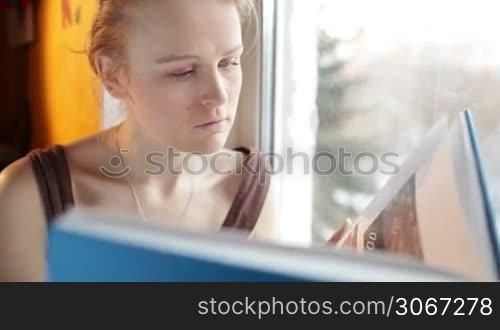 Girl reads a book near window. Close up portrait with natural light and reflector.