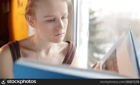 Girl reads a book near window. Close up portrait with natural light and reflector.