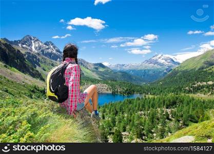 Girl resting during a trek in the mountains watching the view over a lake in the summer