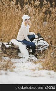 Girl resting on the trunk of a fallen tree covered with snow.. Portrait of a girl sitting in the winter on a fallen tree in the reeds by the la