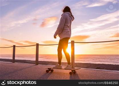 Girl riding a skateboard near the beach at sunset.