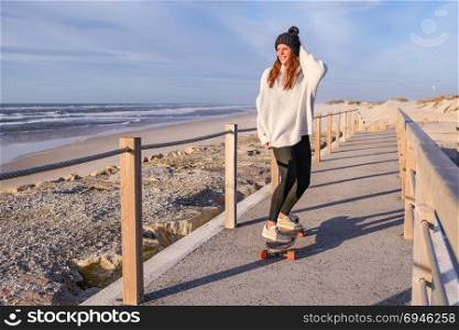 Girl riding a skateboard near the beach at sunset.