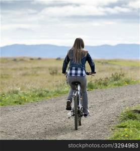 Girl riding bicycle on unpaved country road