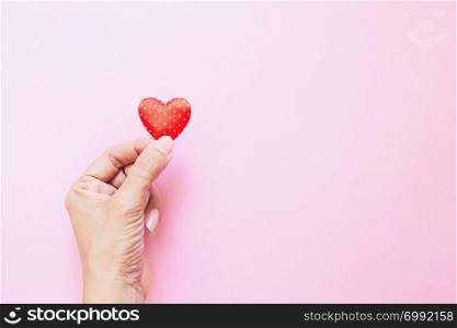 Girl&rsquo;s hand with mini polka dots red heart on pink background with copy space. Valentine&rsquo;s Day. Heart donation. Love concept