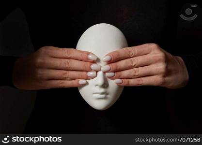 Girl&rsquo;s hands close eyes of plaster mask face on a black background. See no evil. Concept three wise monkeys. Place for text.. Woman&rsquo;s fingers close eyes of gypsum mask face on a black background. See no evil. Concept three wise monkeys.