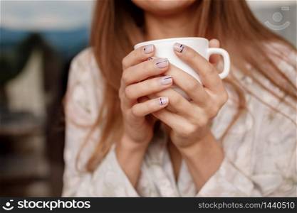 girl&rsquo;s hands holding a white cup with coffee or tea.. girl&rsquo;s hands holding a white cup with coffee or tea