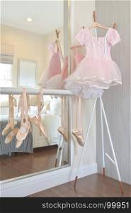 Girl's pink dress and ballet shoes hang on bar in bedroom