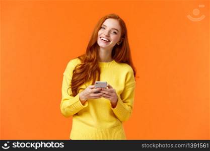 Girl searching gifts for holidays online. Carefree happy redhead female student using smartphone app, laughing joyfully, holding mobile phone, chatting or browsing social networks, orange background.. Girl searching gifts for holidays online. Carefree happy redhead female student using smartphone app, laughing joyfully, holding mobile phone, chatting or browsing social networks, orange background