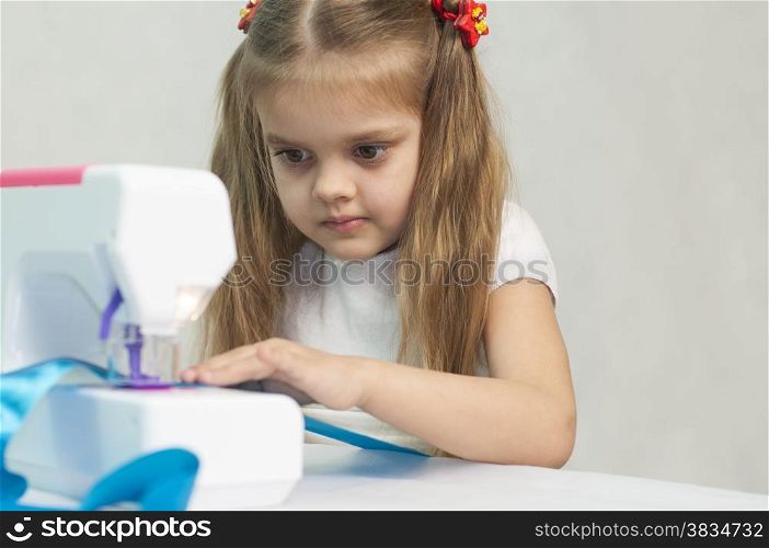 Girl sew on a children&#39;s sewing machine. Studio, a white background.