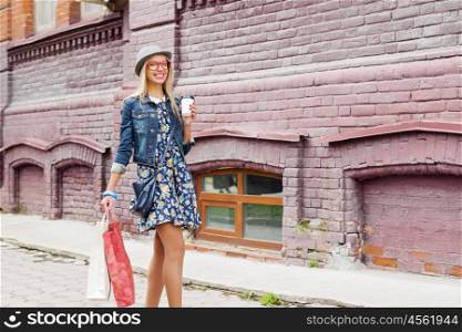 Girl shopping while travel . Happy tourist girl with bags and coffee cup walking on city street