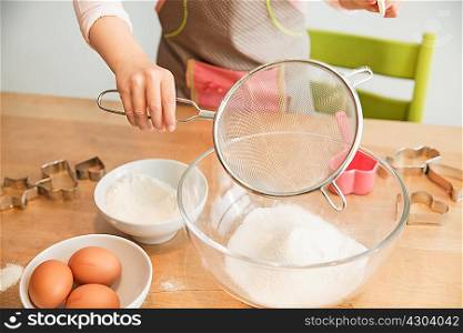 Girl sieving flour into mixing bowl