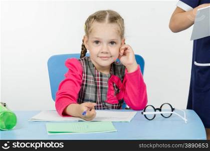 Girl sits at a table on which lay a notebook and writes them. Charming schoolgirl at the desk