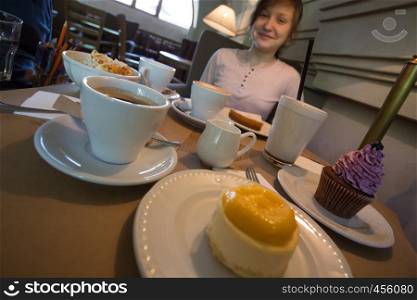 girl sitting at a table in a cafe. cupcakes, cheesecake, coffee