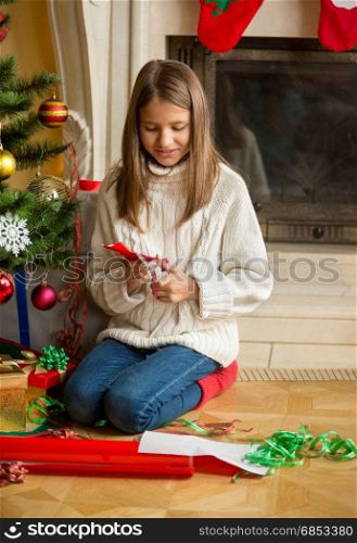 Girl sitting at Christmas tree and cutting snowflakes out of decorative paper