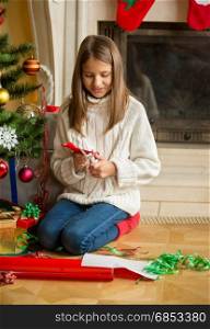 Girl sitting at Christmas tree and cutting snowflakes out of decorative paper