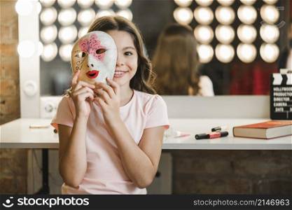 girl sitting backstage holding venetian mask front her face