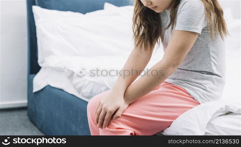 girl sitting bed touching her knees with two hands