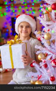 Girl sitting by the Christmas tree with big gifts in her hands