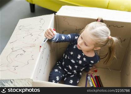 girl sitting cardboard box decorating it with felt tip pen