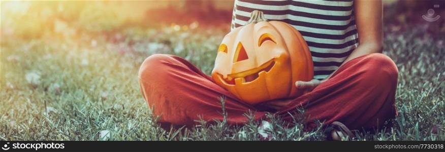 Girl Sitting in Backyard with Nice Carved Pumpkin. Traditional Halloween Decoration. Jack-o-Lantern. Happy Autumn Holiday Background. Halloween Holiday Backgound