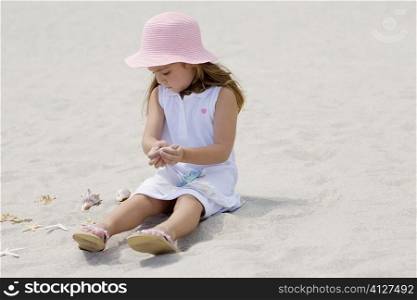 Girl sitting near a starfish and seashells on the beach