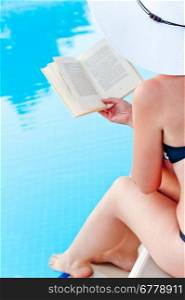 girl sitting near the pool with a book in hand