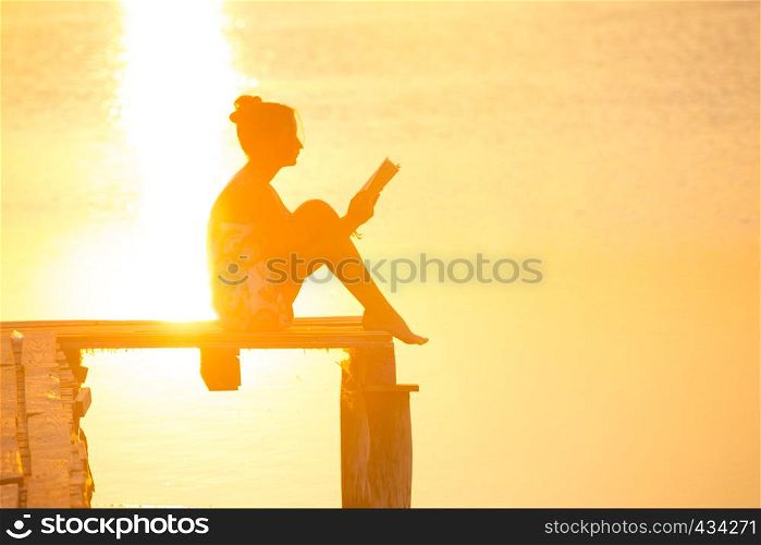 girl sitting on a pier and reading at the sunset time