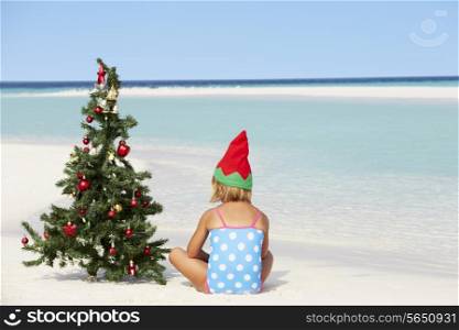 Girl Sitting On Beach With Christmas Tree And Hat