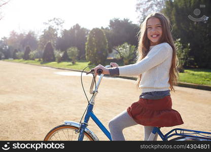 Girl sitting on bicycle in park looking at camera smiling