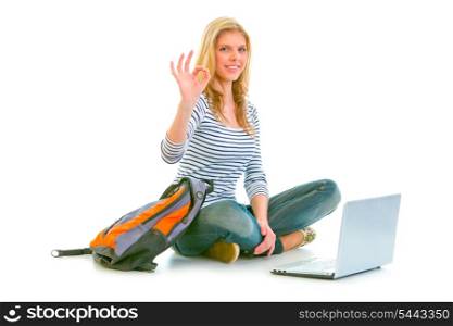 Girl sitting on floor with backpack and laptop showing ok gesture isolated on white &#xA;