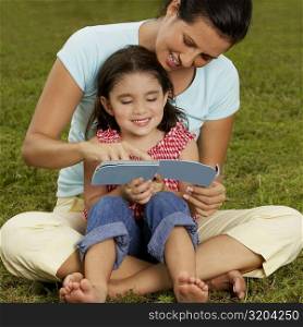 Girl sitting on her mother&acute;s lap and reading a book