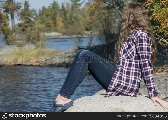 Girl sitting on rock at lakeside, Lake of the Woods, Ontario, Canada