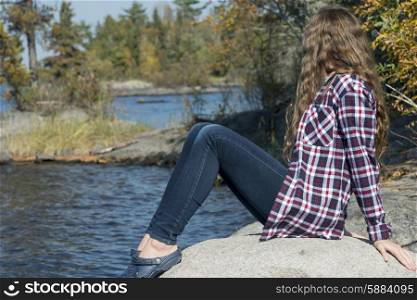 Girl sitting on rock at lakeside, Lake of the Woods, Ontario, Canada