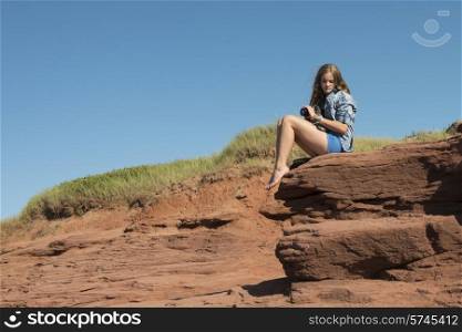 Girl sitting on rock, Cavendish Beach, Green Gables, Prince Edward Island, Canada