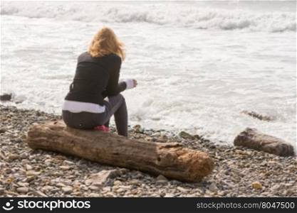 Girl sitting on the log on the coast and looks at sea